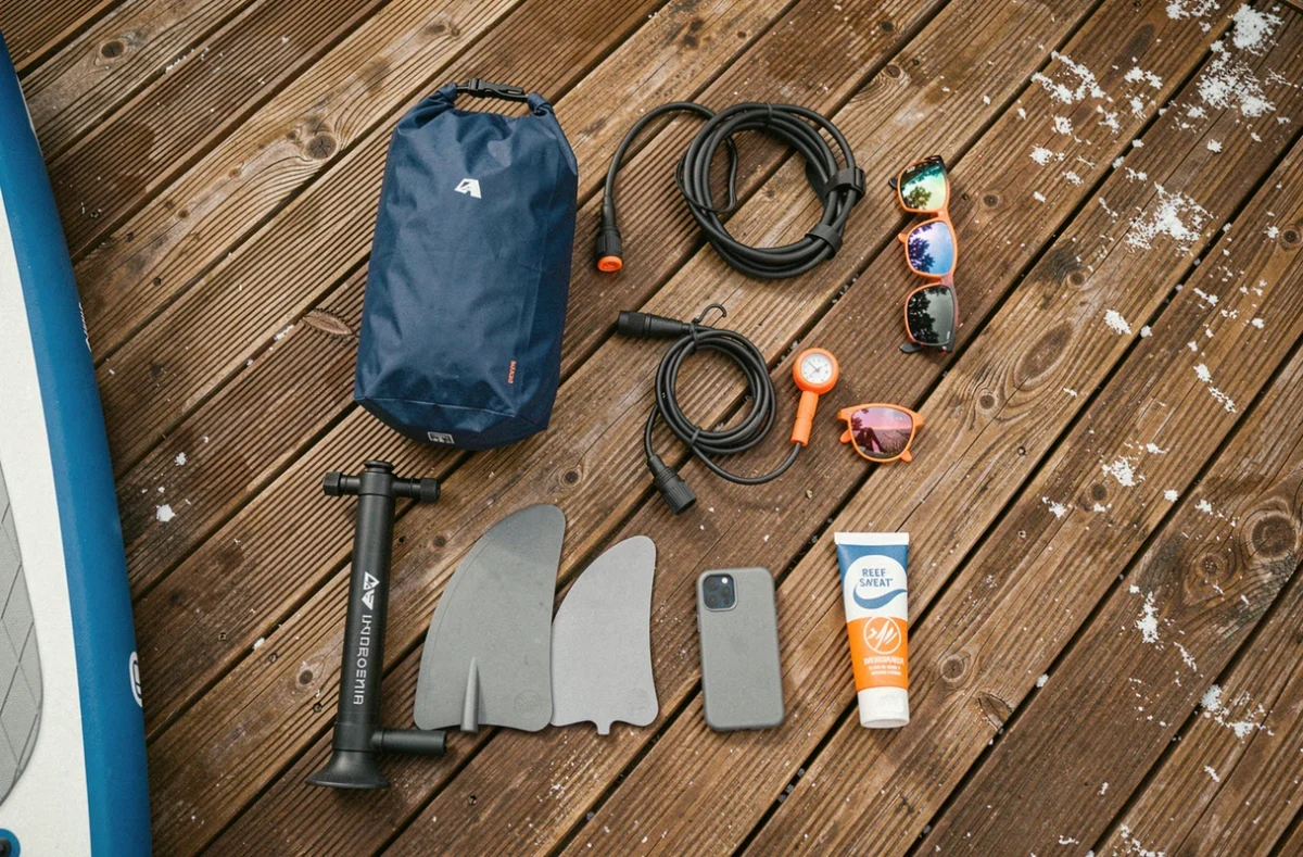Flat-lay des accessoires essentiels pour le stand-up paddle : leash, pompe, sac étanche, aileron et lunettes polarisées
